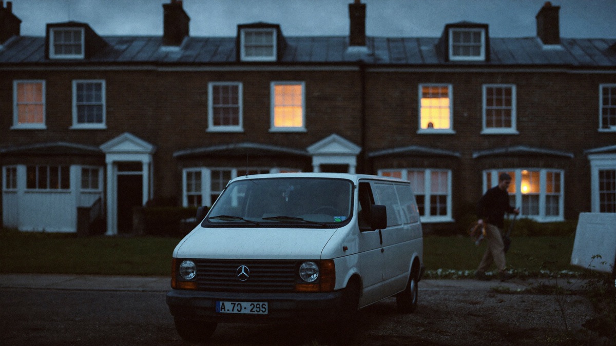 A white work van parked at blue hour outside a brick Manchester terrace, warm light in the windows, a tradesman walking to the door